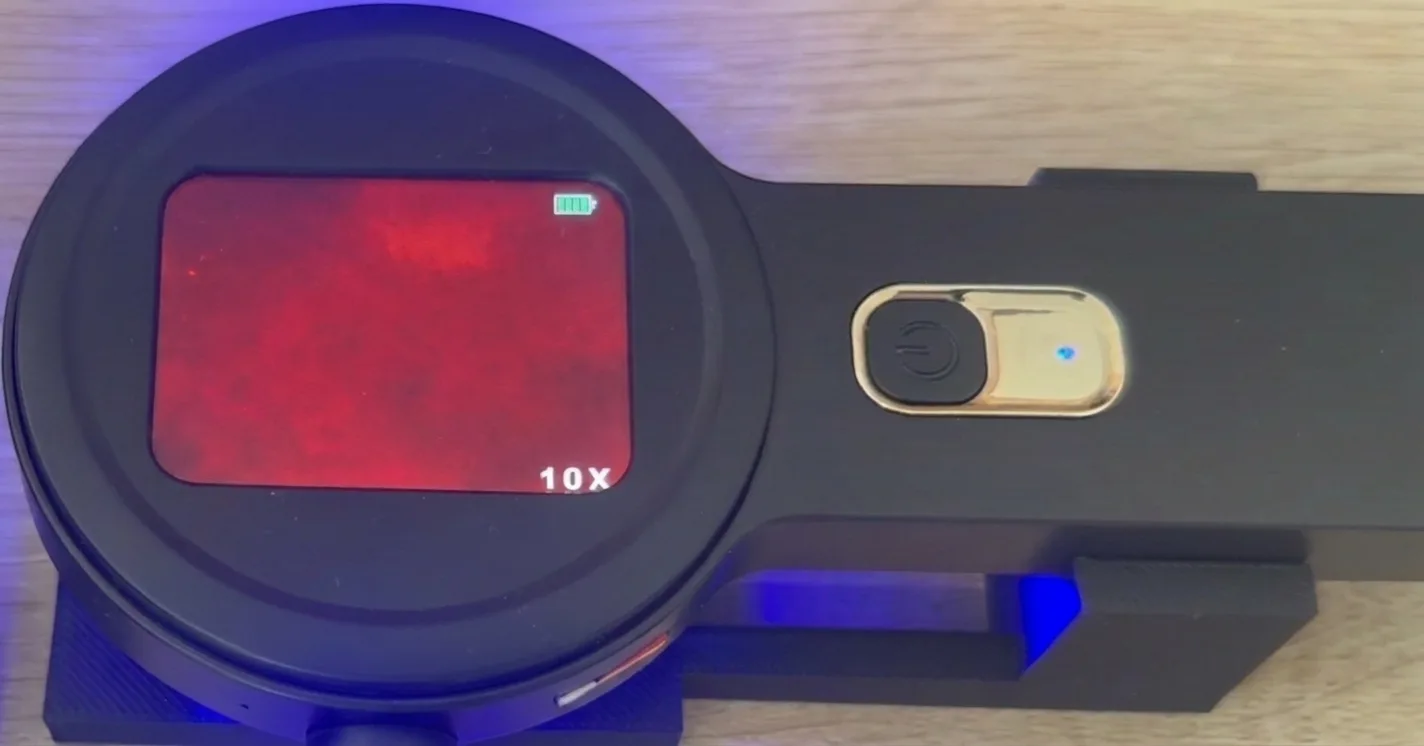 Microscope view with microplastic particles — faint glowing dots on the red field (example 1)