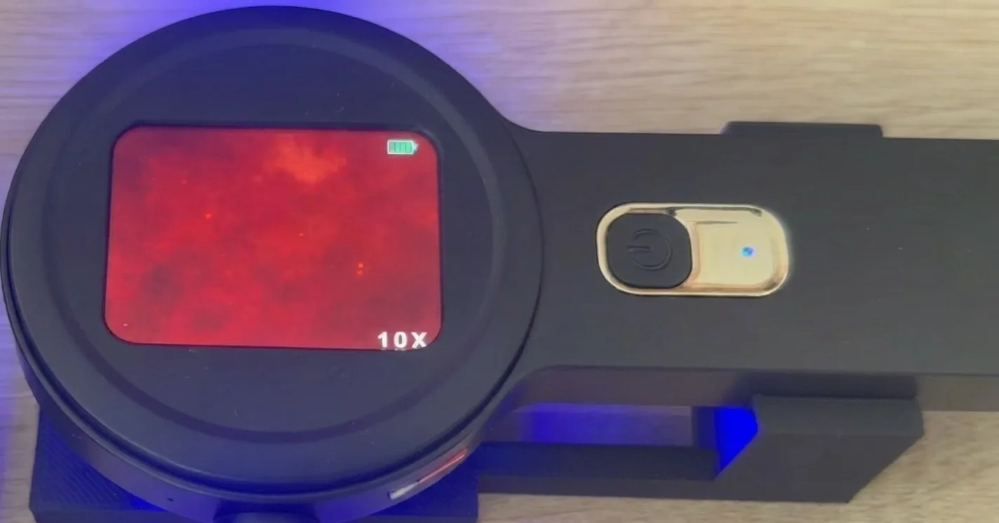 The microscope screen showing microplastic particles as faint glowing dots on a red field