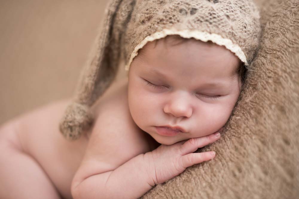 recém-nascida com gorro bege na cabeça em ensaio newborn no estúdio fotográfico laura alzueta em São Paulo