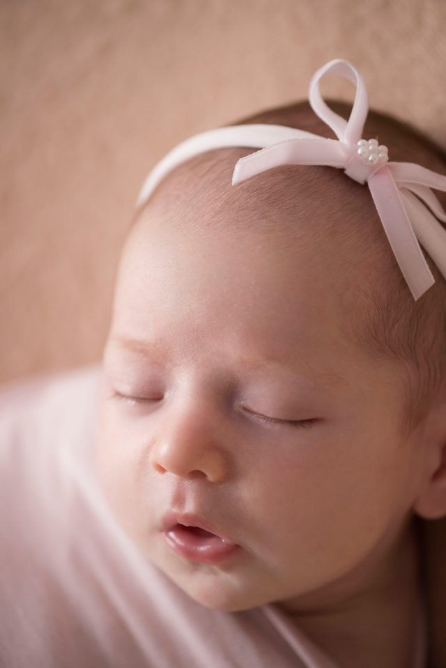 foto de bebê menina enrolada no wrap com laço rosa na cabeça no estúdio de fotografia laura alzueta