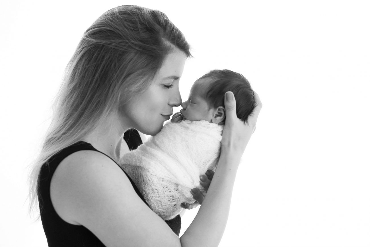 foto preta e branca de mãe beijando filha recém-nascida enrolada em wrap em estúdio de fotografia newborn