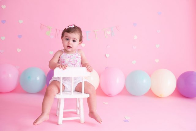 bebê sentada em cadeira com fundo rosa com balões candy colors smash the cake laura alzueta estúdio de fotografia são paulo ensaio de fotos de aniversário de 1 ano de bebê menina