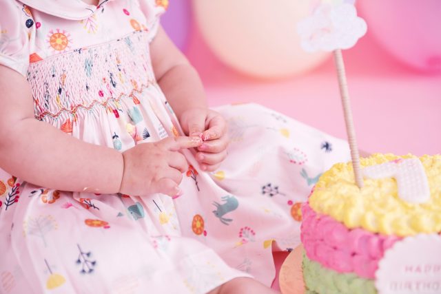 bolo colorido com arco-íris bebê sentada em cadeira com fundo rosa com balões candy colors smash the cake laura alzueta estúdio de fotografia são paulo ensaio de fotos de aniversário de 1 ano de bebê menina