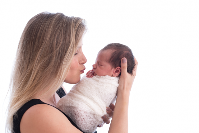 mãe beijando filha recém-nascida enrolada em wrap em estúdio de fotografia newborn fotógrafa laura alzueta pinheiro sp