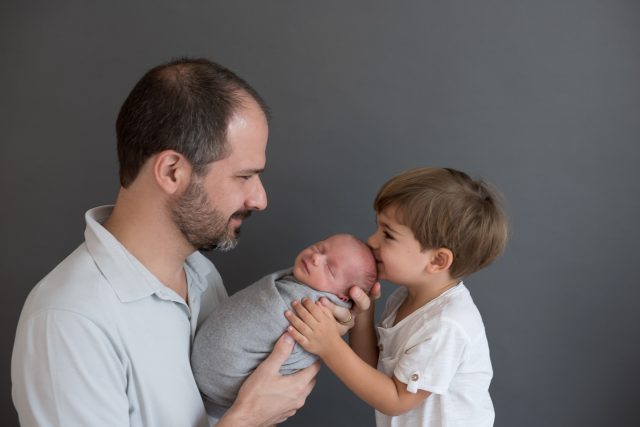 ensaio newborn com irmãos irmão mais velho de 3 anos segurando bebê e dando beijinho com o pai ao lado ensaio fotográfico laura alzueta