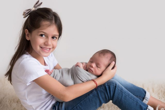 ensaio newborn com irmãos menina segura bebê recém-nascido