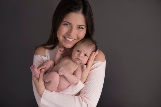 mãe sorri segurando bebê recem nascida ensaio newborn