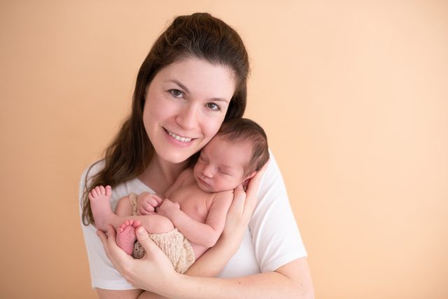 mãe segura bebê no colo recém nascido em fundo bege composição de fotos para ensaios newborn de menino
