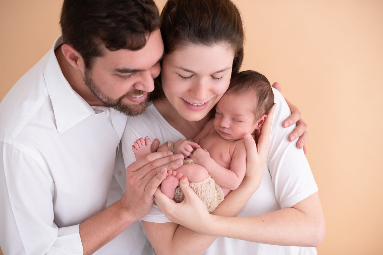 foto de família com recém nascido mãe e pai olhando para bebê composição para fotos de ensaio newborn de menino laura alzueta estúdio fotográfico em são paulo