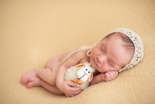 foto de bebê segurando ursinho de pelúcia recém nascido com touca na cabeça composição com cores neutras newborn de menino