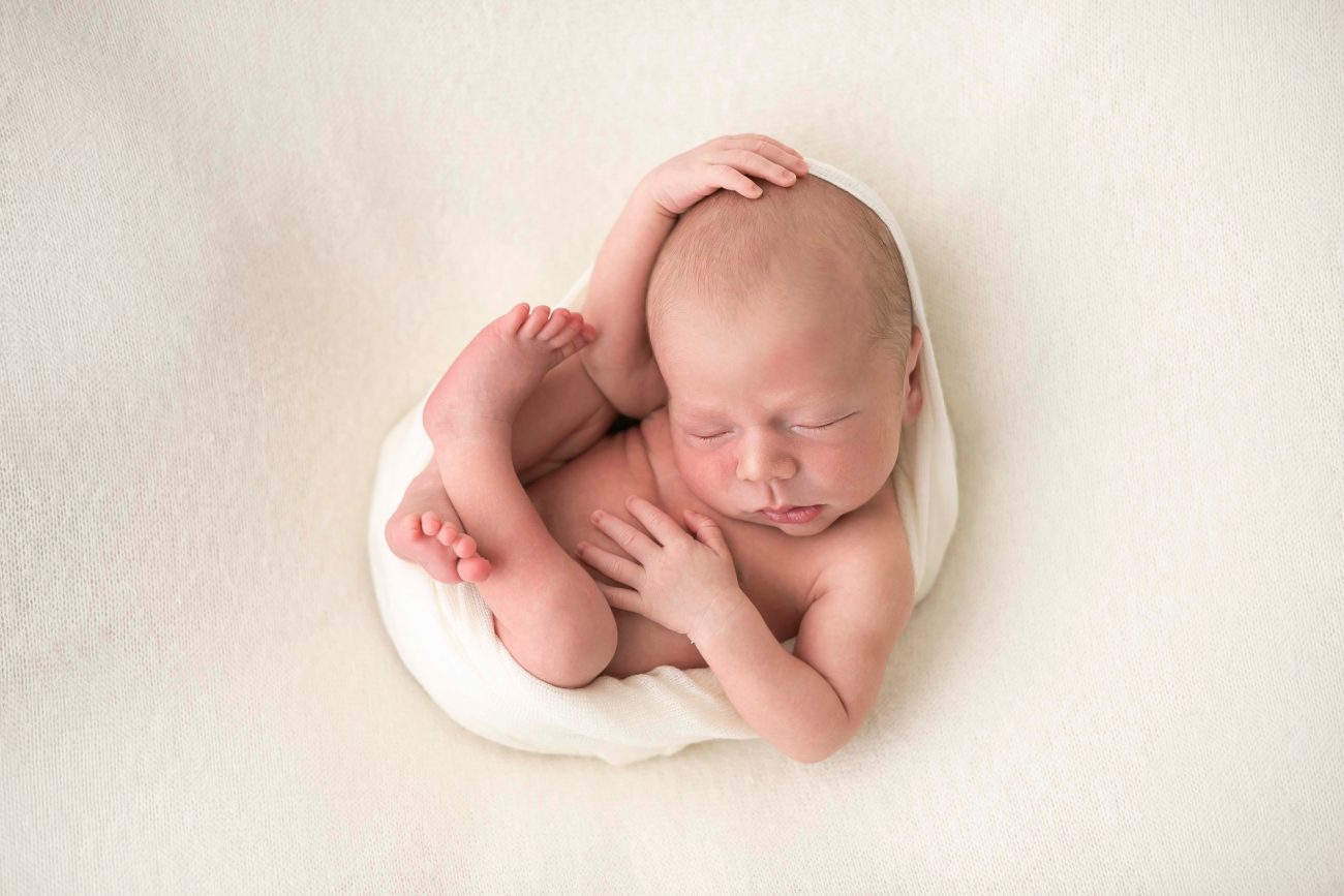 bebê enrolado em wrap branco deitando no pufe fotos de ensaio newborn de menino composição fotografia laura alzueta são paulo