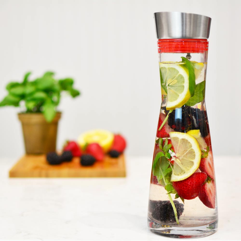 Grosche-rio-sangria bottle-water-and-fruit-infuser-being-held-on-white-marble-counter-and-fruit-in-background