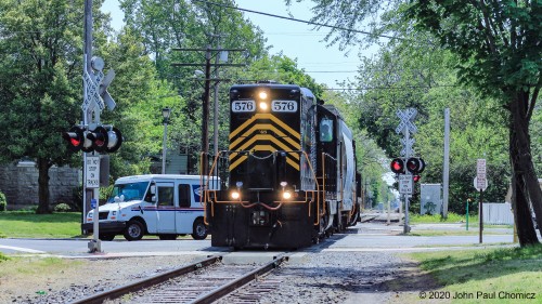 With unit #: 576 leading, long hood forward, train #: J101 crosses North 3rd Street, in Millville, on its way back north to Millville Yard with empties from Durand Glassworks.