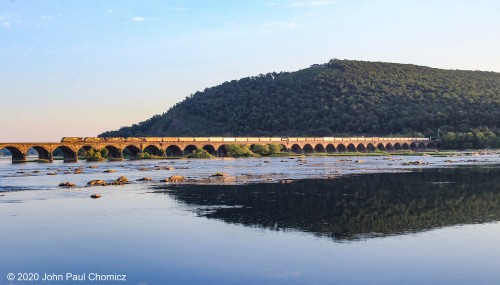 A lengthy, eastbound, mixed freight heads out of Enola and crosses over the Rockville Bridge in a scene that is beautifully lit by the setting sun.