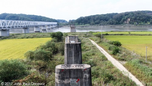 This is a view looking north, across the DMZ, into North Korea. In the foreground are the bullet riddled remains of the original rail bridge, which linked both Koreas, and was destroyed during the war. On the left is the new bridge that was constructed, along with Dorasan Station, in 2002, when the political situation between the two Koreas seemed a bit brighter. With the recent re-escalation of tensions between the two, the new bridge sits unused and is as much a of scar from the war as the remains of the original bridge.