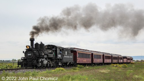 The, "Antonito Limited", train departs at 10am sharp and is two minutes out of the depot in this photo as it parallels County Road 12.5 in Antonito, CO. This location is famous as it was featured at the beginning of the movie Indiana Jones and the Last Crusade. In the scene, young Indiana Jones rides his horse alongside a circus train and climbs aboard to escape his pursuers.