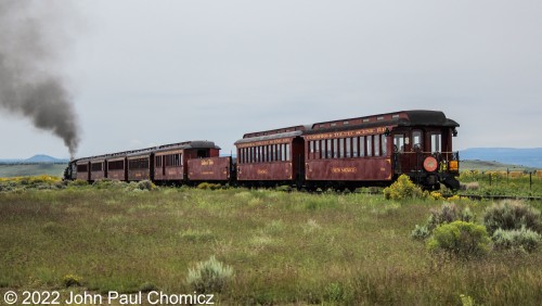 A rear view of the passing, "Antonito Limited", train as it leaves the city limits and approaches the beautiful hills of Colorado and New Mexico beyond.