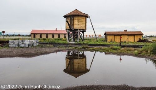 A puddle from the previous night's rain storm reflects the water tower that quenches the thirst of the Cumbres & Toltec Scenic Railroad's steamers in Antonito, CO.