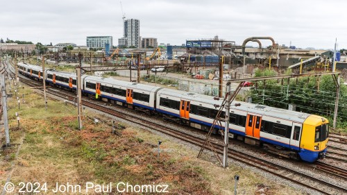 A zoomed-out view of the same London Overground train operating diesel-powered through an overhead catenary zone.