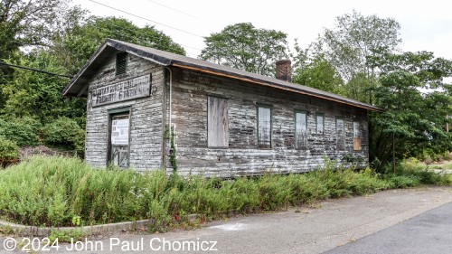 That tiny forlorn freight station is the Raritan River Railroad Station and is the last surviving station of that shortline railroad. It was built in the early 1900's and had a prosperous run as a passenger station before the effects of the Great Depression took their toll on the railroad service through the area. With the exception of a brief period during World War 2, the railroad service through this station never recovered.